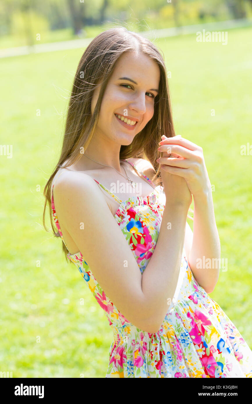 Portrait of young beautiful woman with long hair wearing flower dress in green spring park Stock Photo