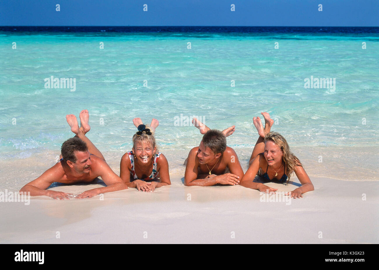 Two couples lie on the abdomen on the white beach, at the background sea Stock Photo