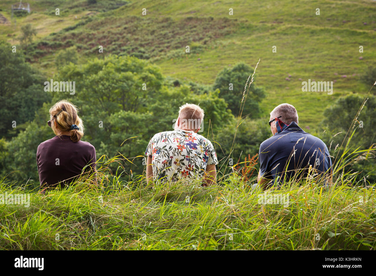 Three people sitting on a grassy  bank Stock Photo