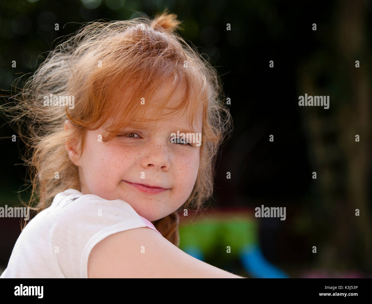 Young girl with red hair looking into Camera against a dark background, backlit Stock Photo