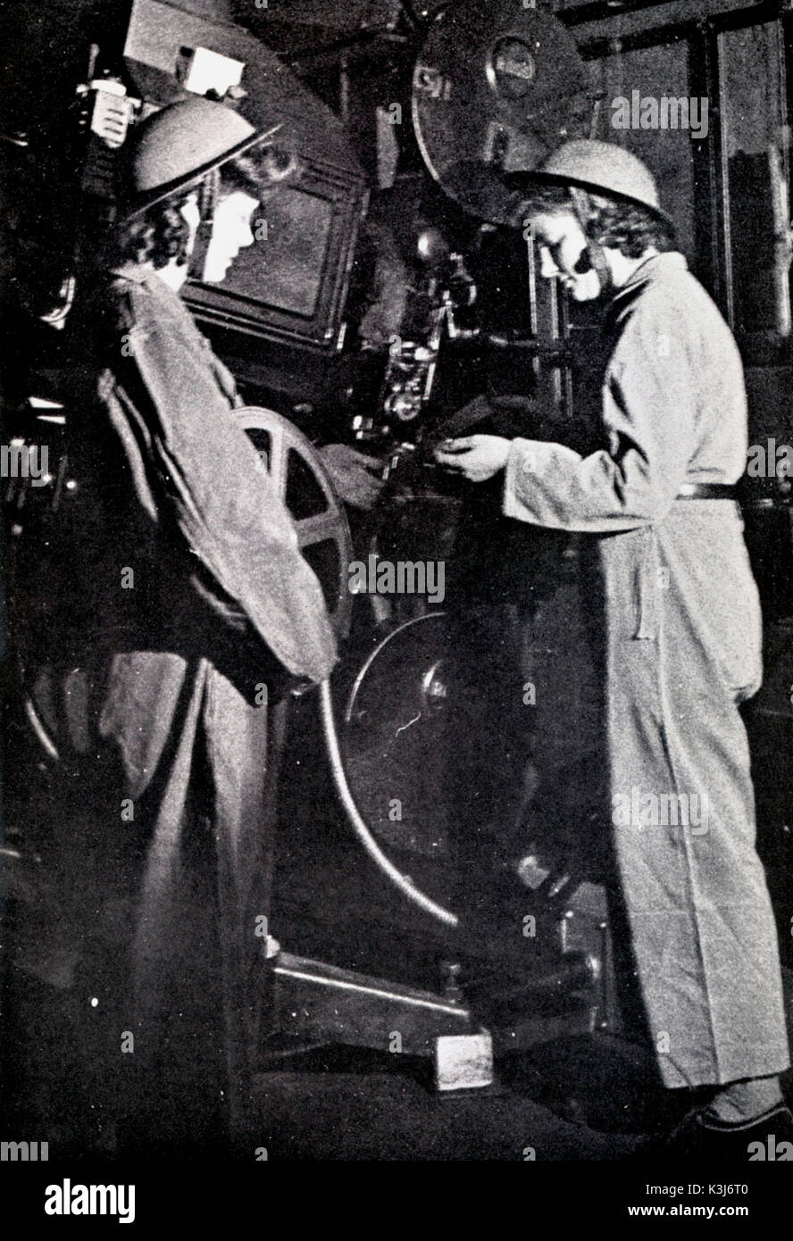 WOMEN PROJECTIONISTS during World War II. Seen here at the Granada Cinema, Harrow, London. Lit for the photograph by having the second projector arc lamp door open, one projectionist checks that the next reel her colleage has brought through, is the correct one. The helmets indicate that air bombing raids were current or expected WOMEN PROJECTIONISTS during World War II. Seen here at the Granada Cinema, Harrow, London. Lit for the photograph by having the second projector arc-lamp door open , one projectionist checks that the next reel her colleague has brought through, is the correct one. The Stock Photo