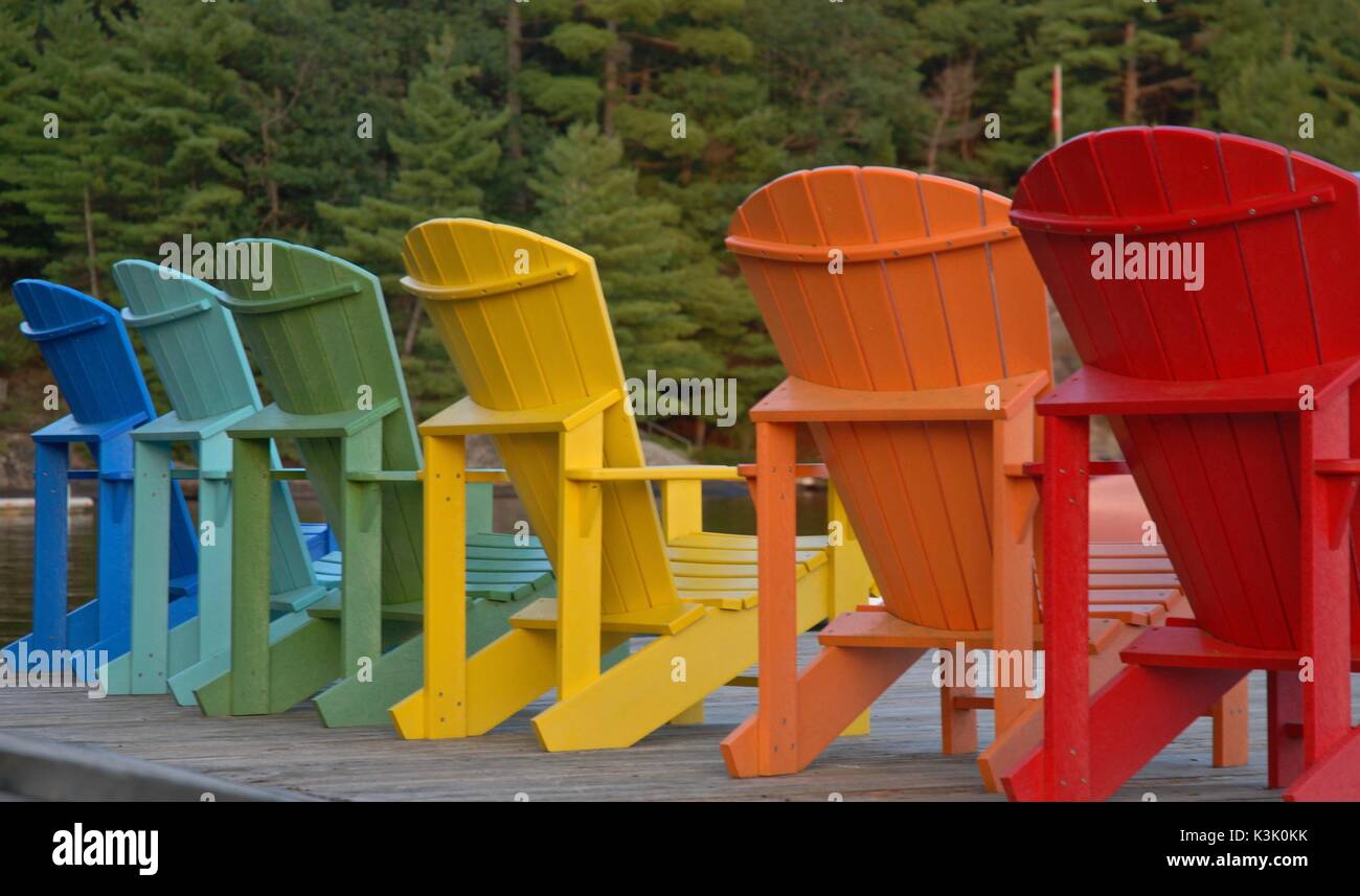 Multi coloured adirondack/muskoka chairs on a wooden dock by the lake