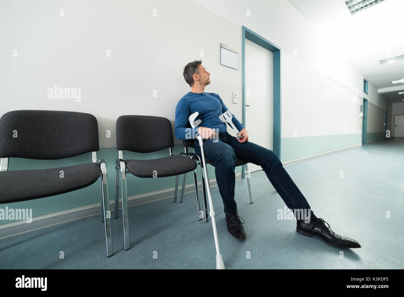 Midadult Man With Crutches Sitting On Chair In Hospital Stock Photo