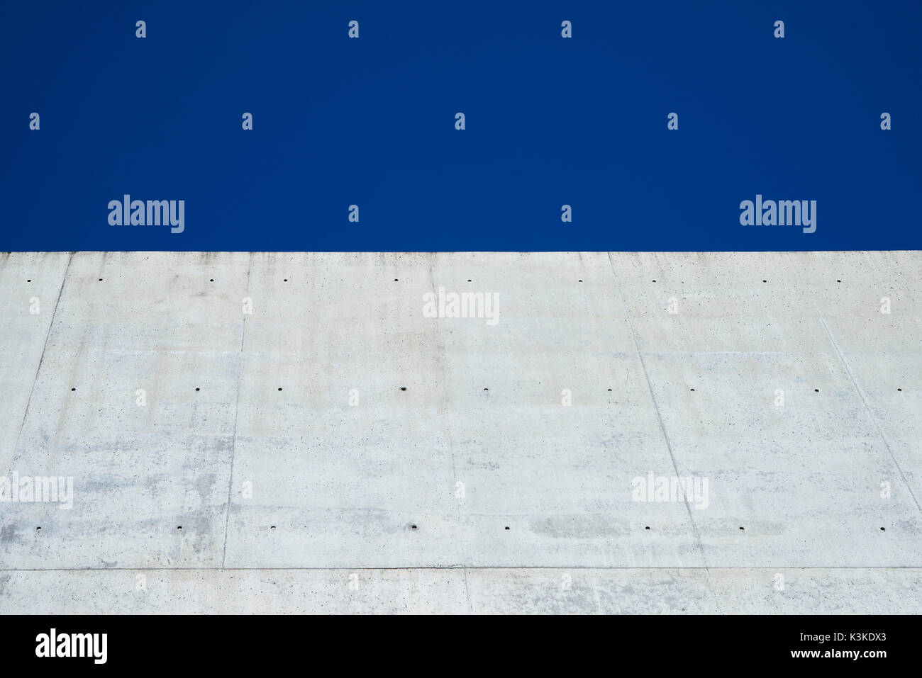 Concrete grey wall with structure and inclusions as a background in front of sky blue cloudless Stock Photo