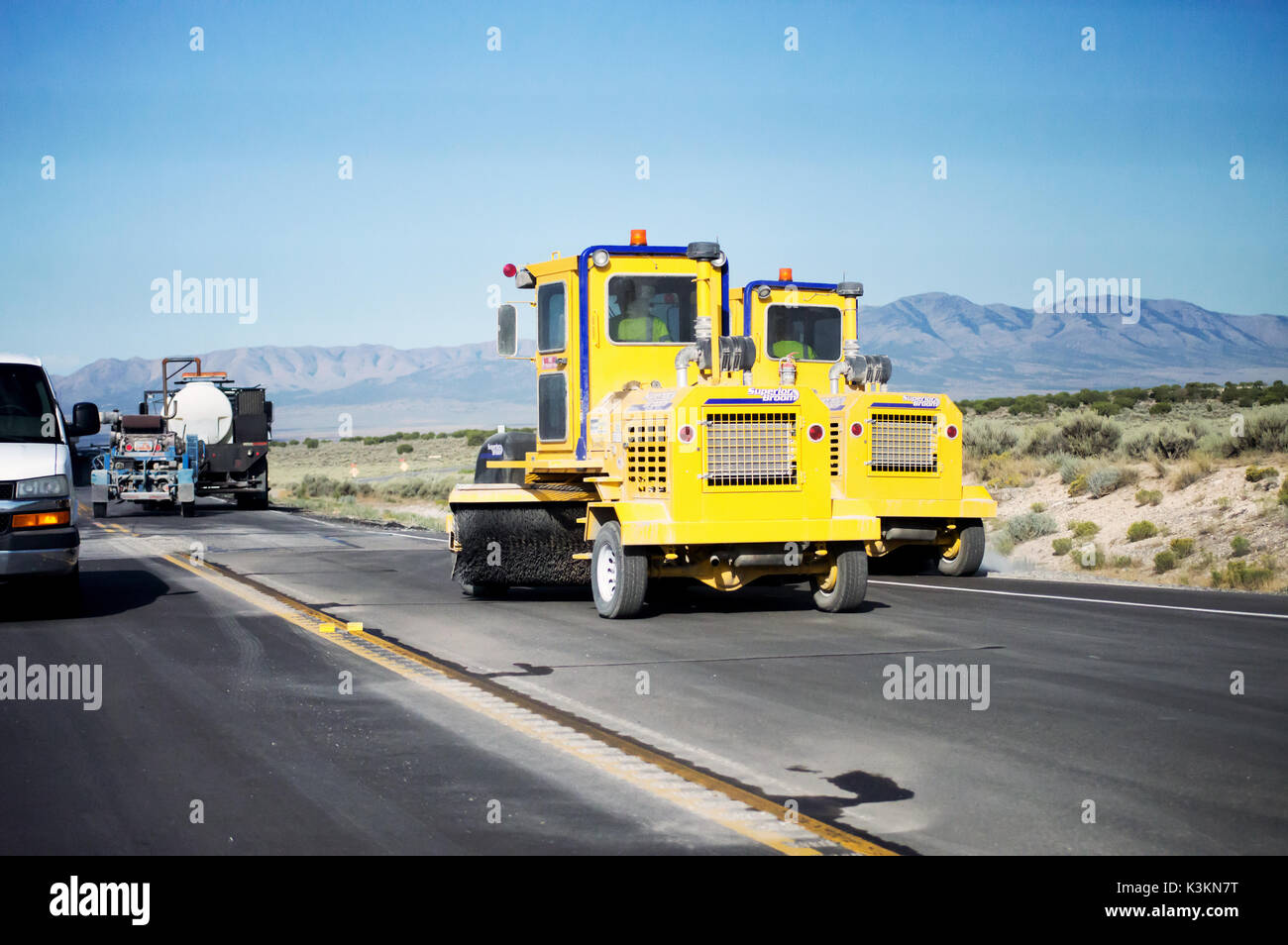 Two yellow street sweepers cleaning a road in the desert for resurfacing. Stock Photo