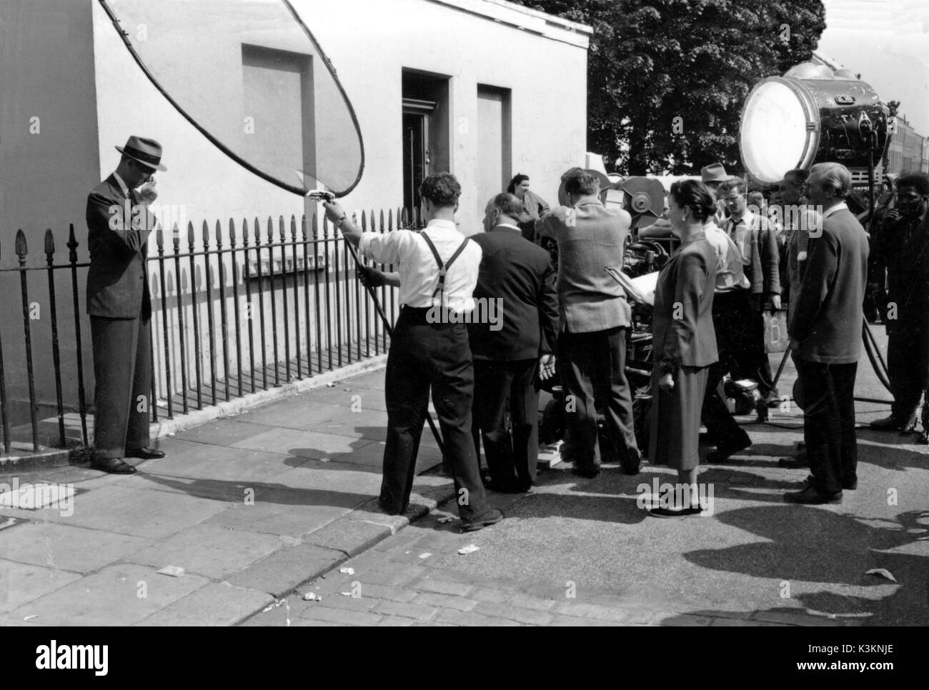 THE MAN WHO KNEW TOO MUCH  On location in Camden Town, London, leading actor JAMES STEWART , Director ALFRED HITCHCOCK [immediately right of man in white shirt and braces], and Technical Advisor CONSTANCE WILLIS [standing, centre right], and beyond her can be glimpsed the Technicolor camera        Date: 1956 Stock Photo