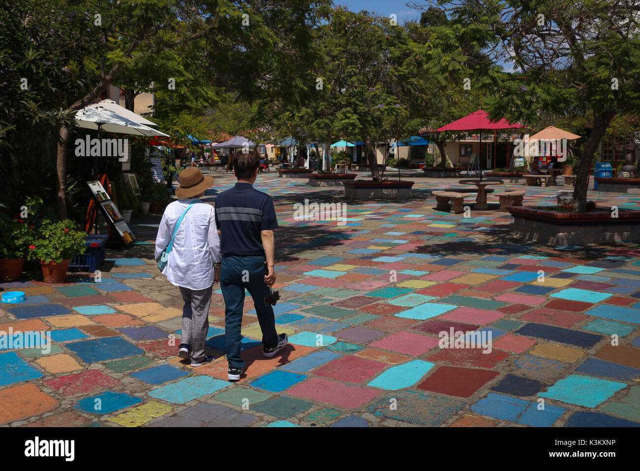 Couple walks hand-in-hand across the colorfully painted pavers of the Spanish Village Art Center plaza in Balboa Park, San Diego, CA in August, 2017. Stock Photo