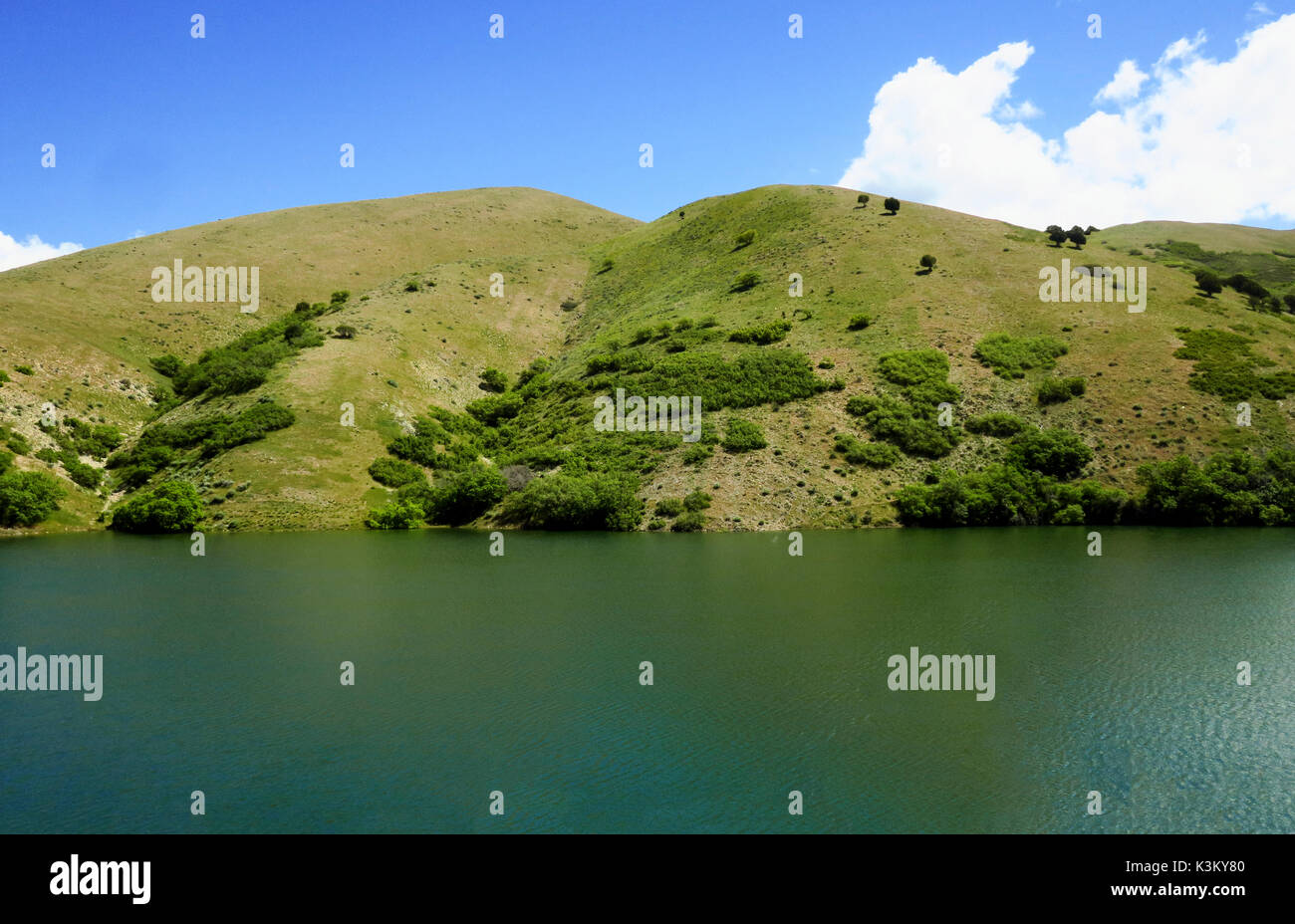 A still, glossy lake in front of a green hillside Stock Photo