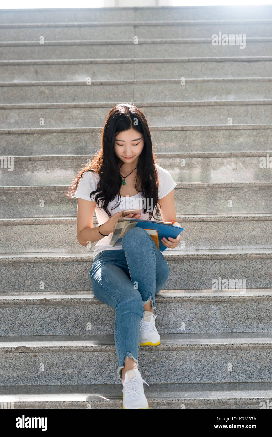 Asian female students using its  smartphone in the Campus aisle Stock Photo