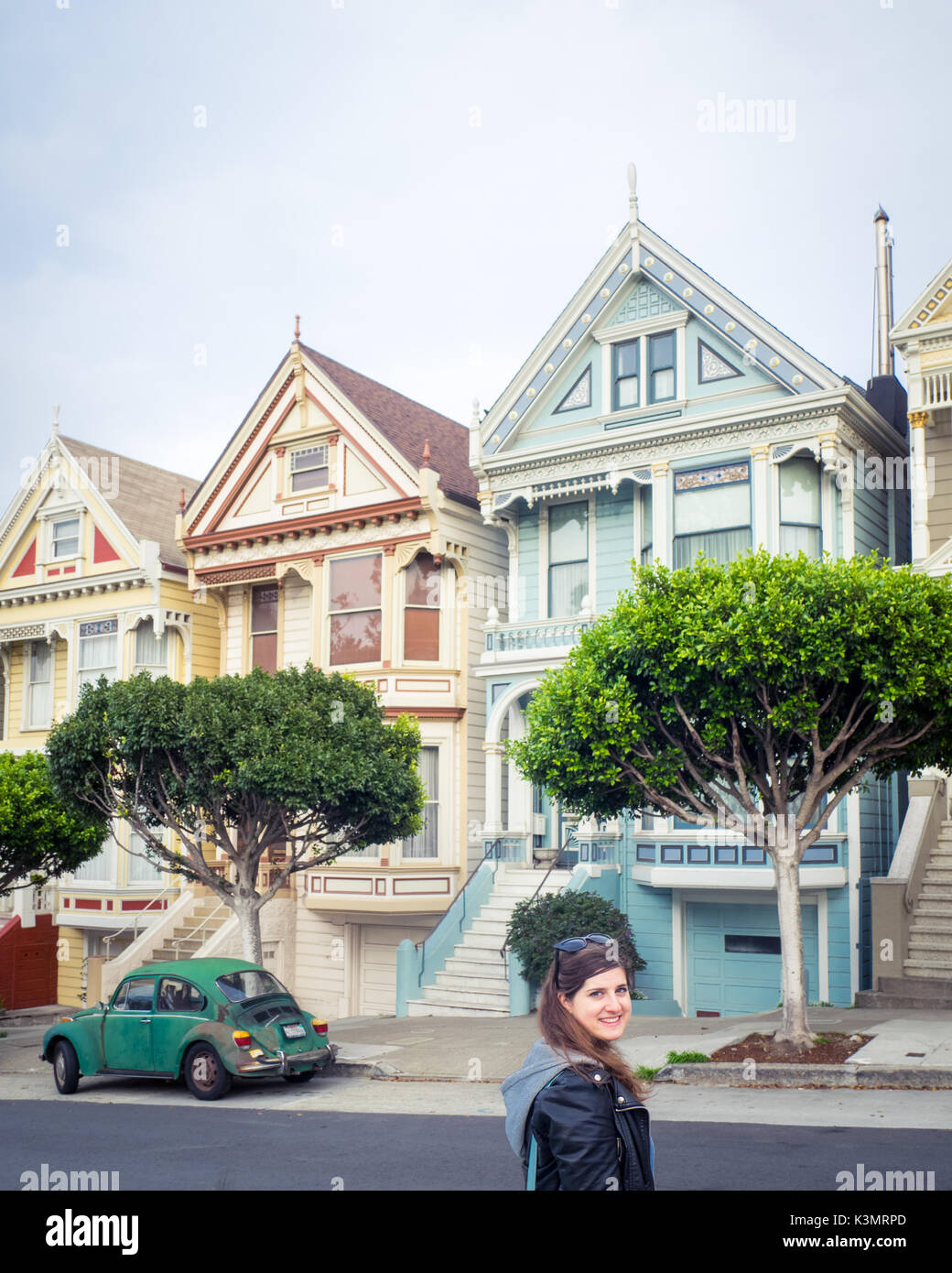 A girl and green Volkswagen Beetle in front of the 'Painted Ladies' row of Victorian Houses on Steiner Street (at Alamo Square) in San Francisco. Stock Photo
