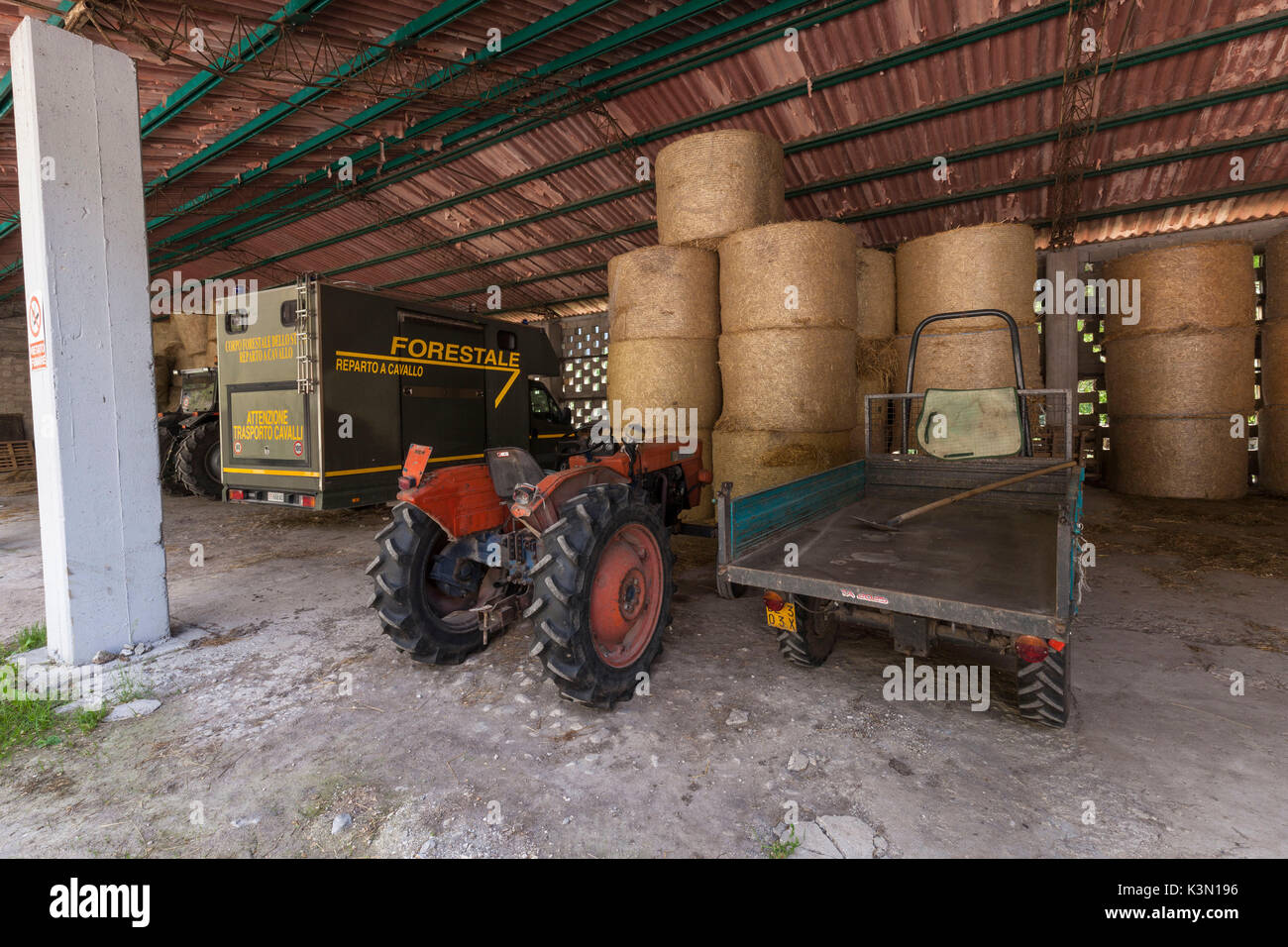 Tractors, equipment and bales of hay in the shed in front of the stables of Case Salet, State Natural Reserves, Monti del Sole Stock Photo
