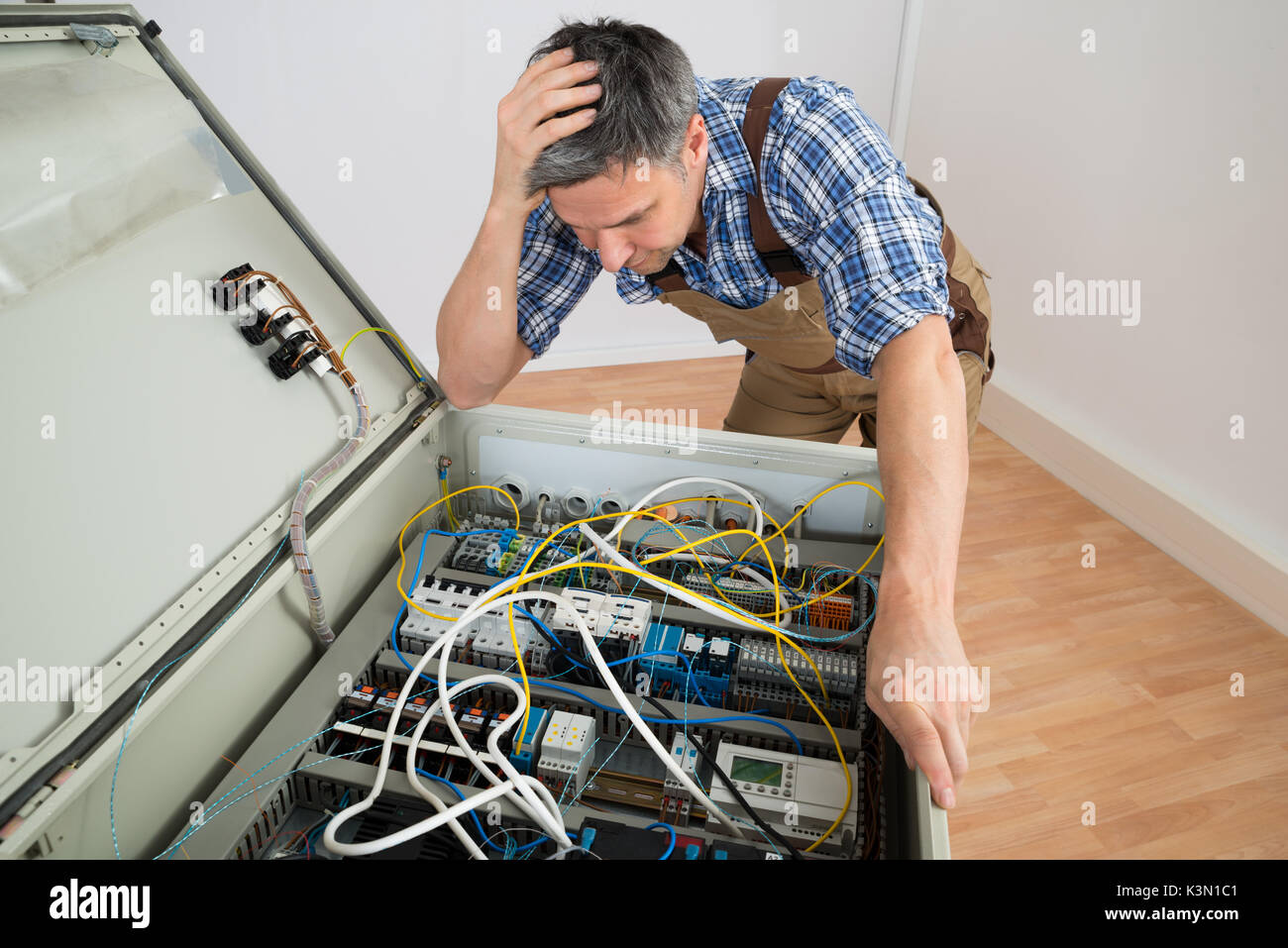 Portrait Of A Confused Electrician Looking At Fuse Box Stock Photo