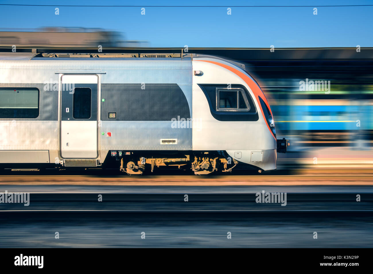 High speed train in motion at the railway station at sunset in Europe. Modern intercity train on the railway platform with motion blur effect.  Moving Stock Photo