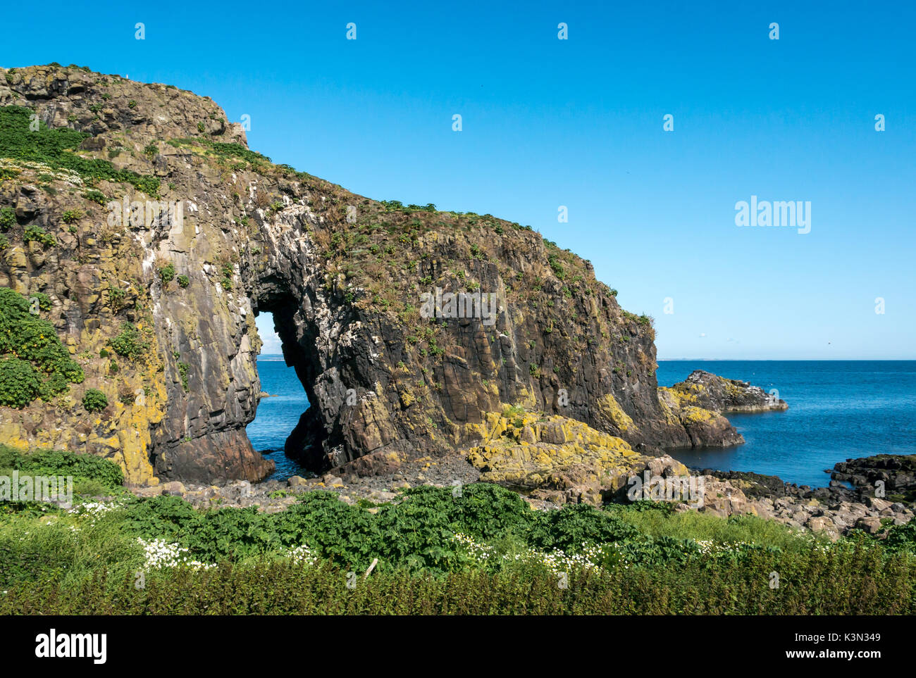 Looking through a natural sea worn arch called the ‘lady in the veil’, Fidra Island, Firth of Forth Scotland UK on a sunny day with blue sky Stock Photo