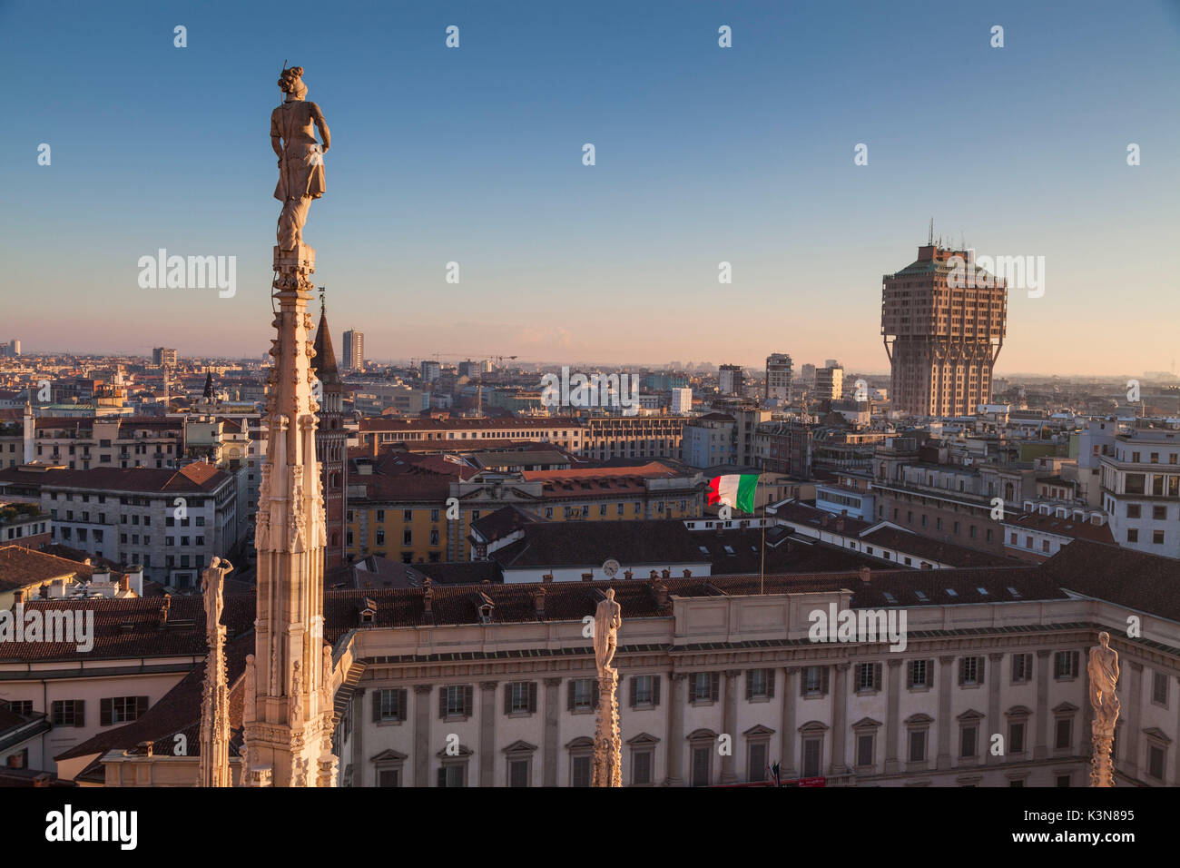 Milan, Lombardy, Italy. View of Velasca tower from the roof of Cathedral's Milan at sunset. In foreground there is a statue Stock Photo