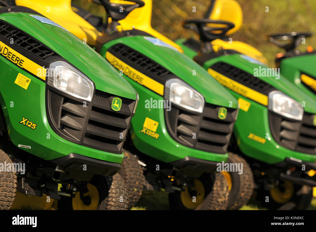 A row of ride on lawn mowers for sale at a show agricultural gardening implements for a large garden tractors style lawn care and mowing Stock Photo