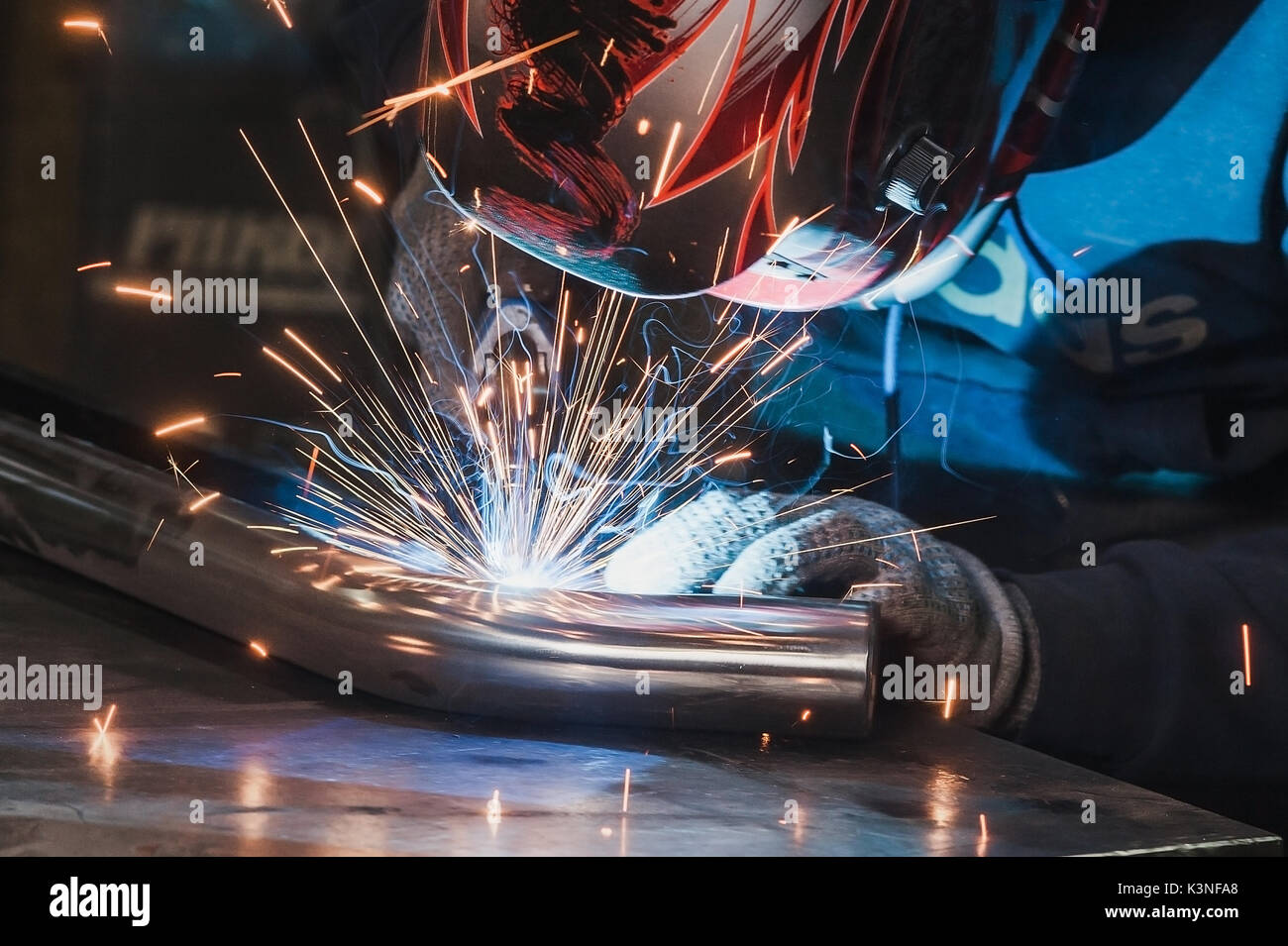 Welder in a steep welding mask welds metal parts with a lot of sparks Stock Photo