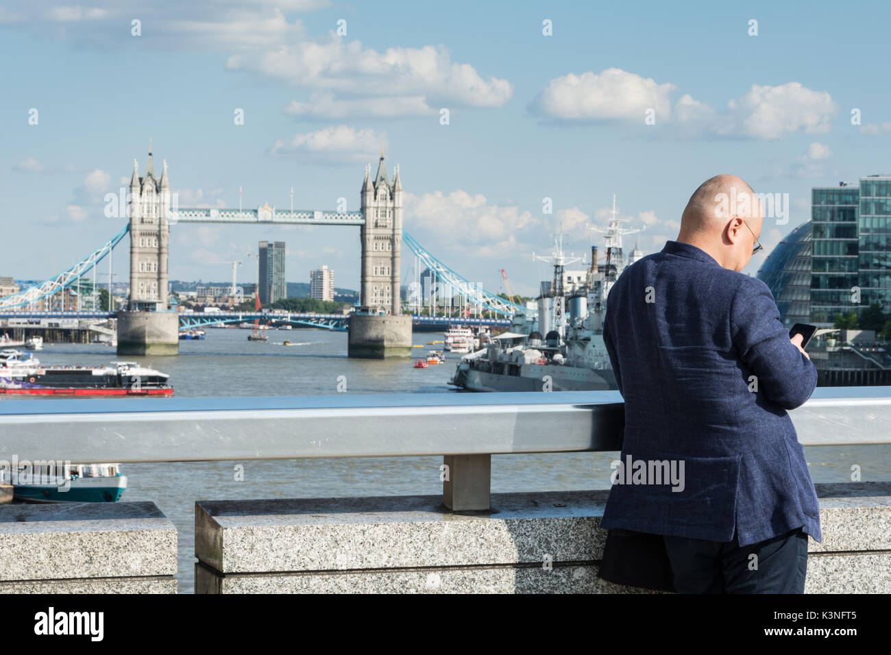 A Chinese businessman on London Bridge taking a photo of Tower Bridge. Stock Photo