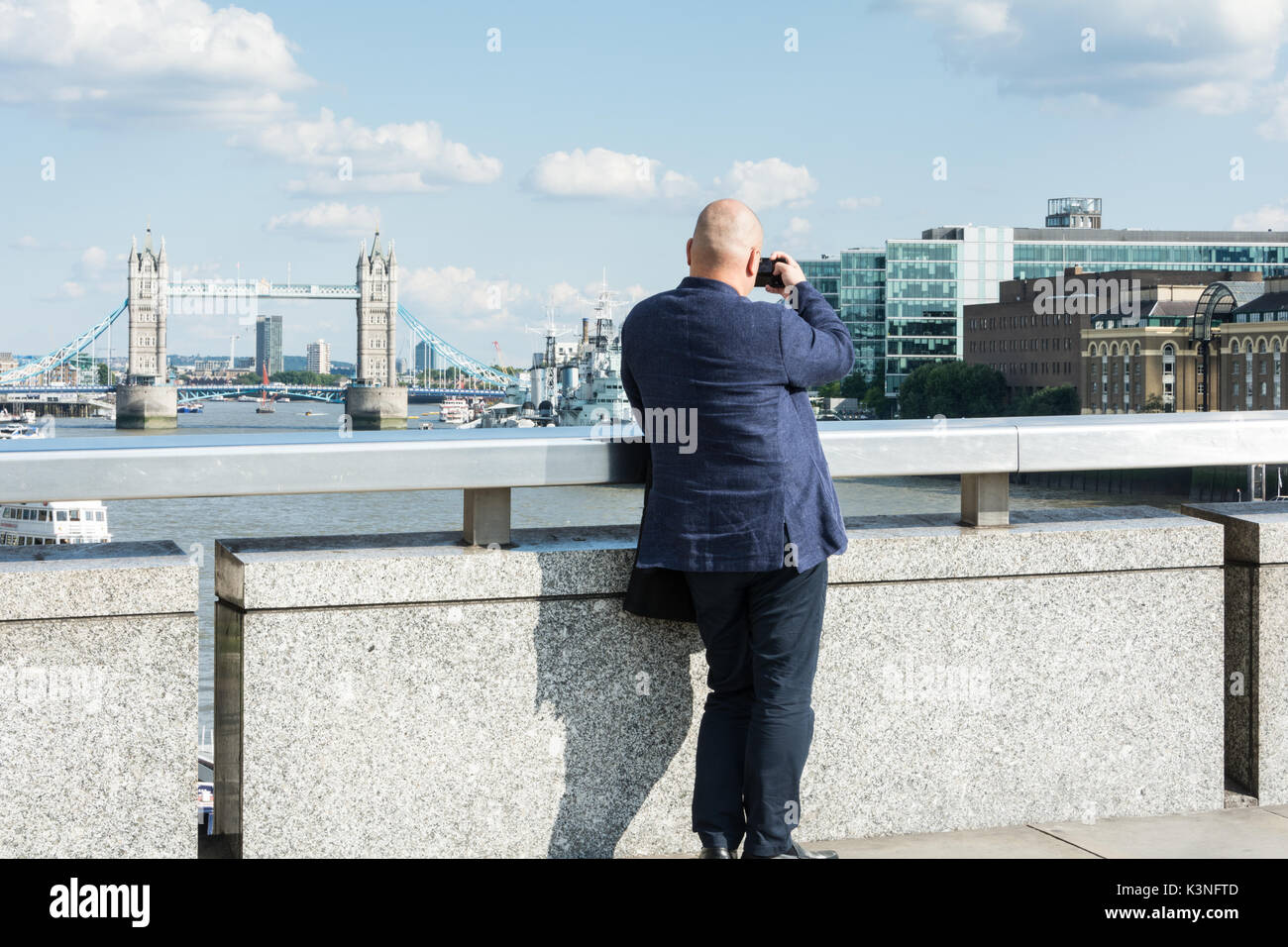 A Chinese businessman on London Bridge taking a photo of Tower Bridge. Stock Photo
