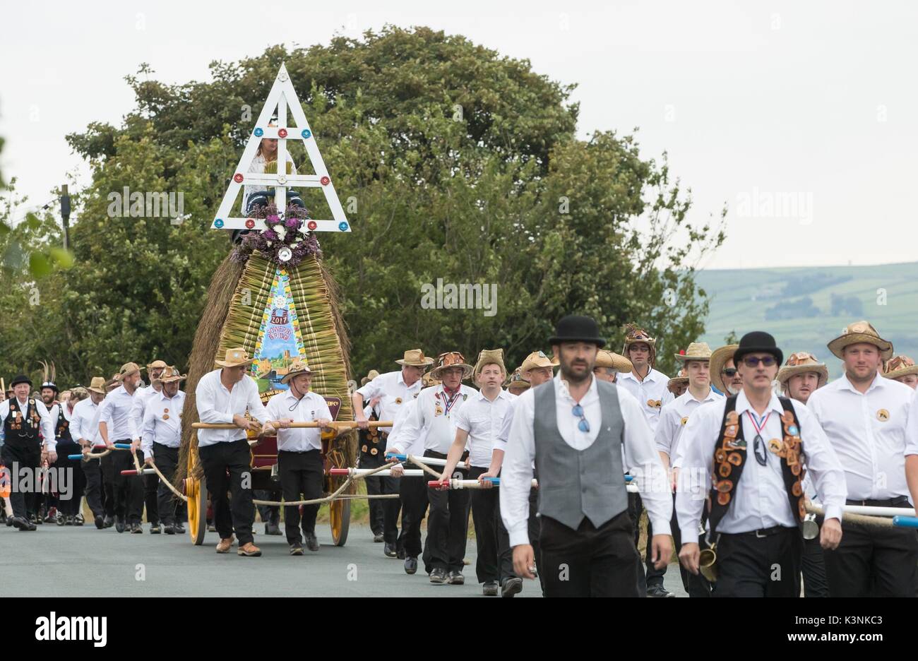 Members of a Rushbearing procession dressed in Panama hats and white shirts lead a sixteen foot high thatched rushcart, a tradition with origins dating back centuries, during the Sowerby Bridge Rushbearing Festival in Yorkshire. Stock Photo