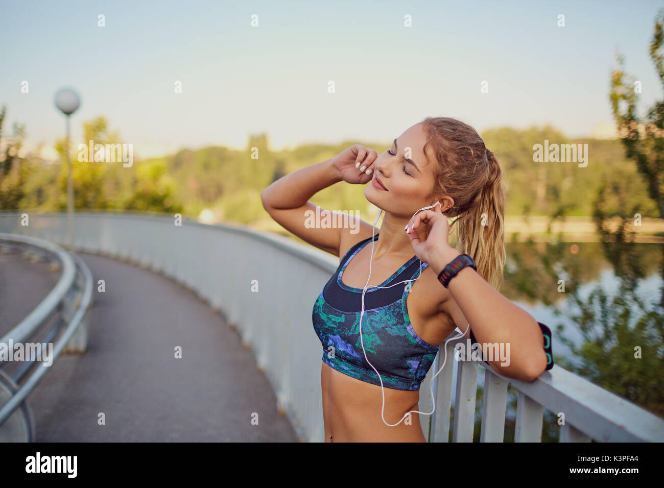 A happy girl jogger listens to music on headphones on a road. Stock Photo