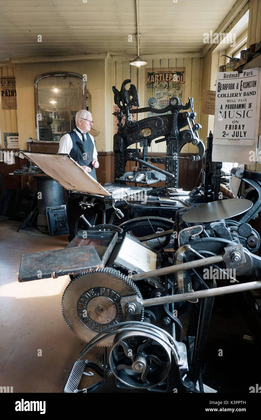 older male printer working vintage flatbed letterpress printing press surrounded by vintage letterpress printing machinery Stock Photo