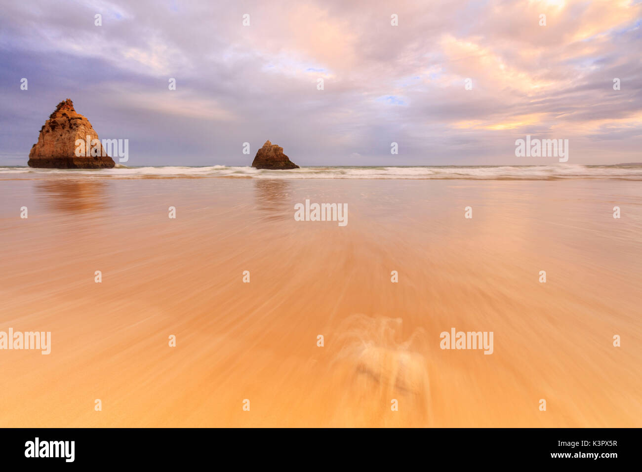 Pink sky at sunset on cliffs and sandy beach surrounded by the clear sea Praia Dos Tres Irmaos Portimao Algarve Portugal Europe Stock Photo