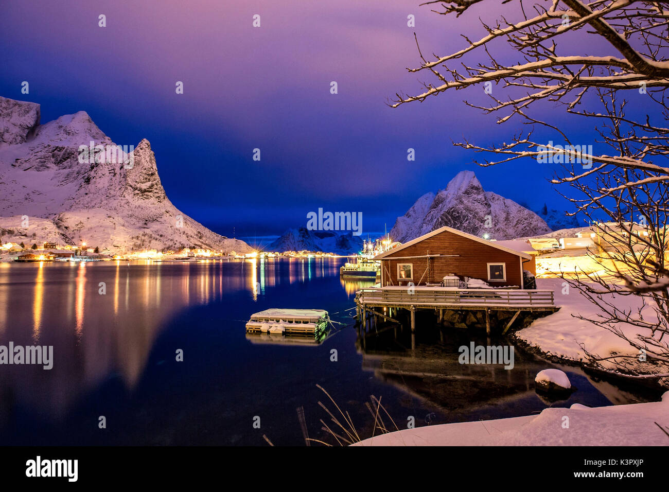A rorbu, the typical Norwegian fishermen house, reflecting in the still water of the sea at the blue hour in Reine, Lofoten islands, Norway. Europe Stock Photo