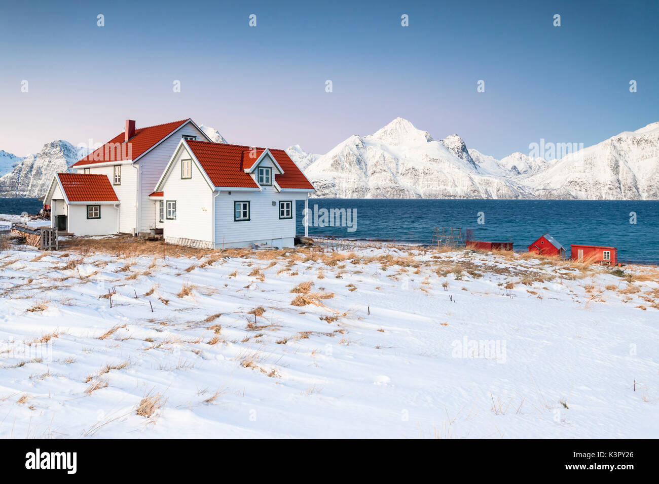 Blue sky on the wooden huts called Rorbu framed by frozen sea and snowy peaks Djupvik Lyngen Alps Tromsø Norway Europe Stock Photo