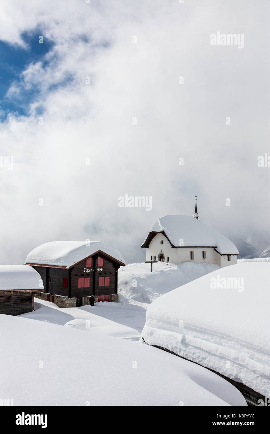 Snow covered mountain huts and church surrounded by clouds Bettmeralp district of Raron canton of Valais Switzerland Europe Stock Photo