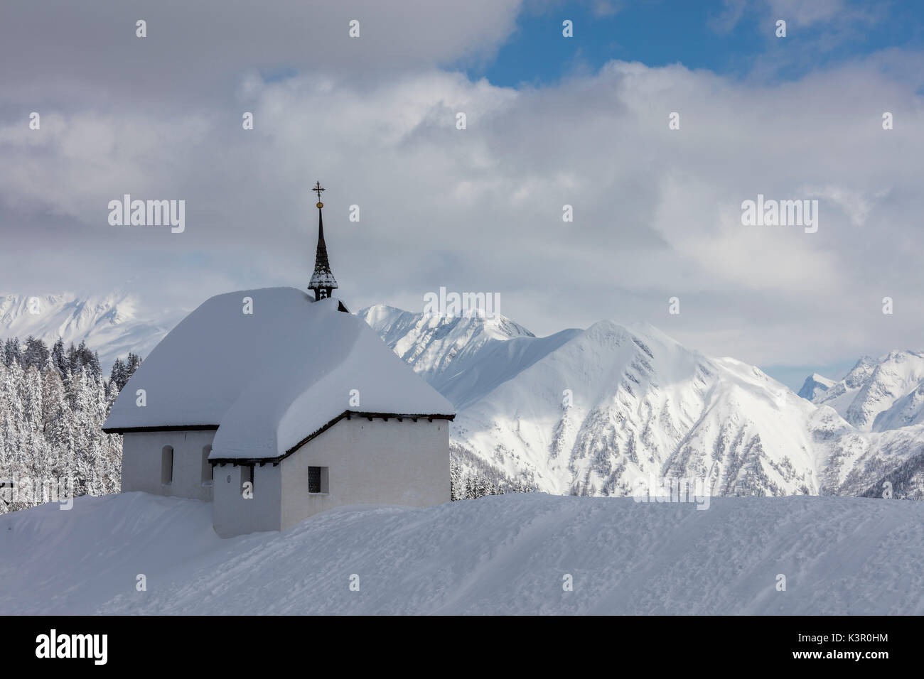 The alpine church immersed in snow frames the high peaks Bettmeralp district of Raron canton of Valais Switzerland Europe Stock Photo
