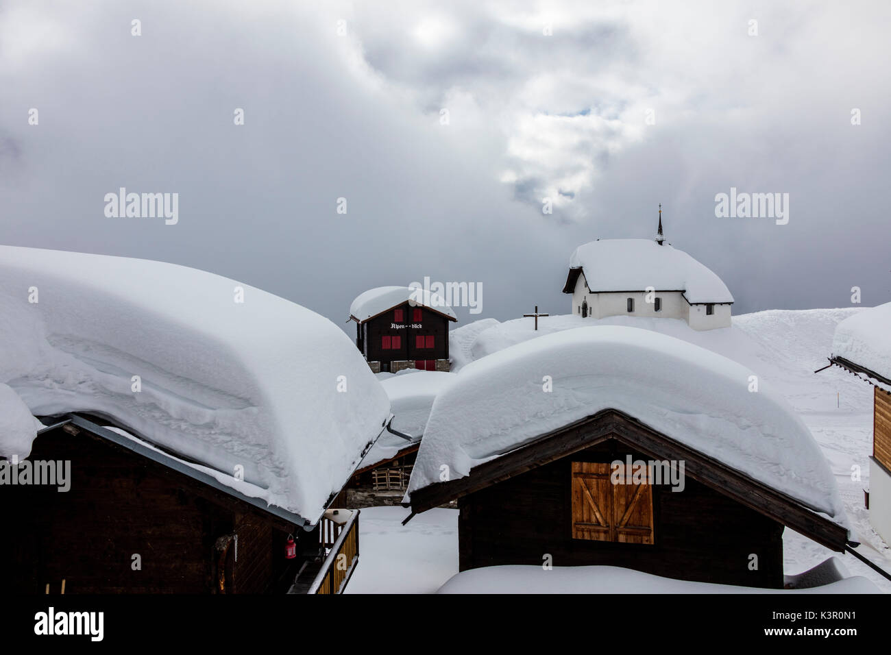 Clouds frame the mountain huts and church covered with snow Bettmeralp district of Raron canton of Valais Switzerland Europe Stock Photo