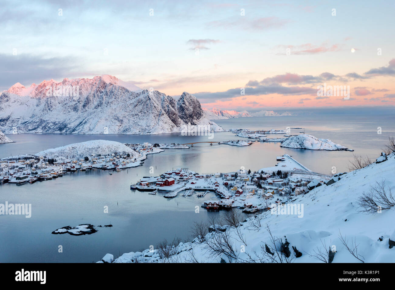 The pink colors of sunset and snowy peaks surround the fishing villages Reine Nordland Lofoten Islands Norway Europe Stock Photo
