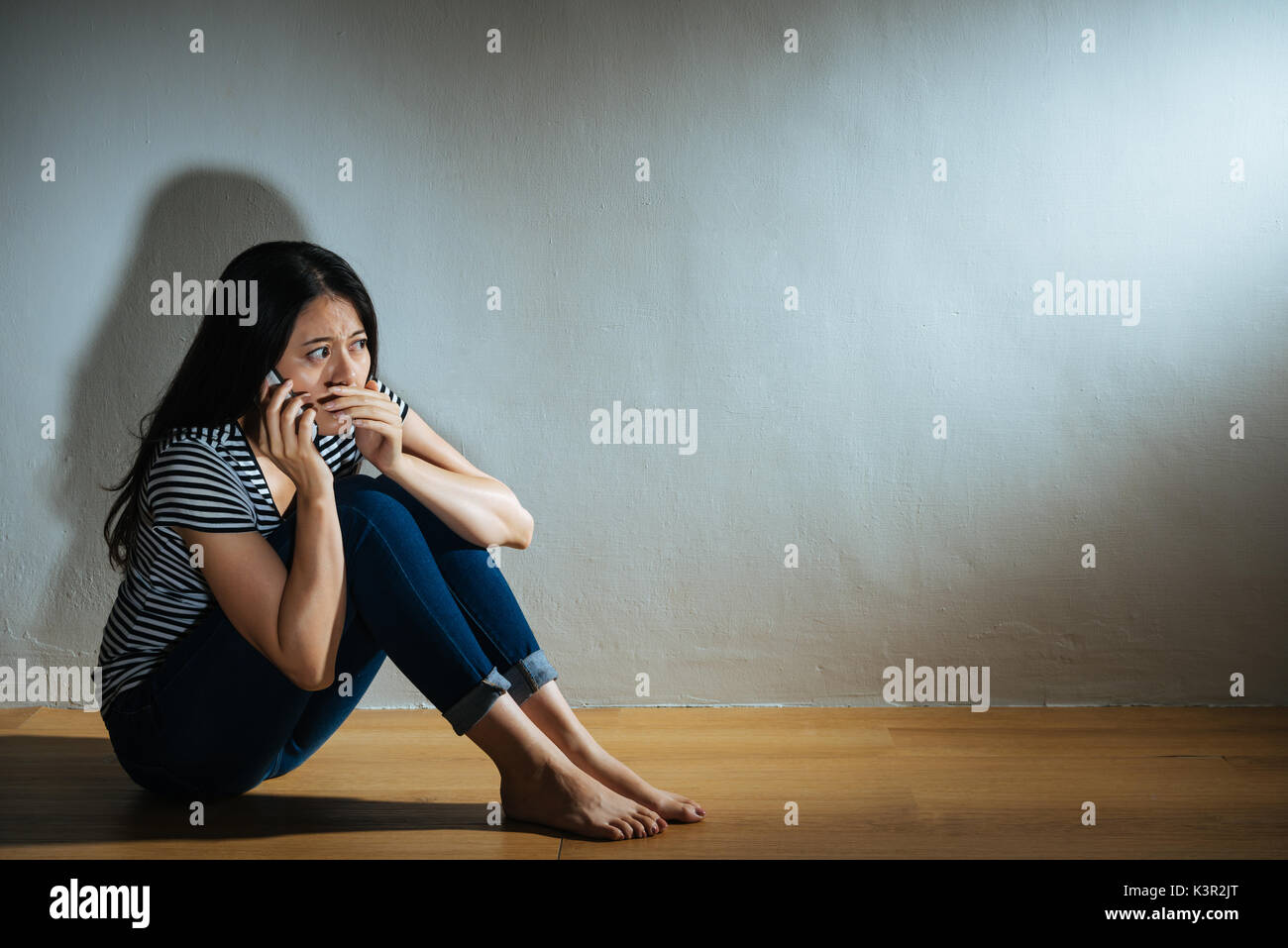 young victim girl sitting on wooden floor using mobile phone calling ...