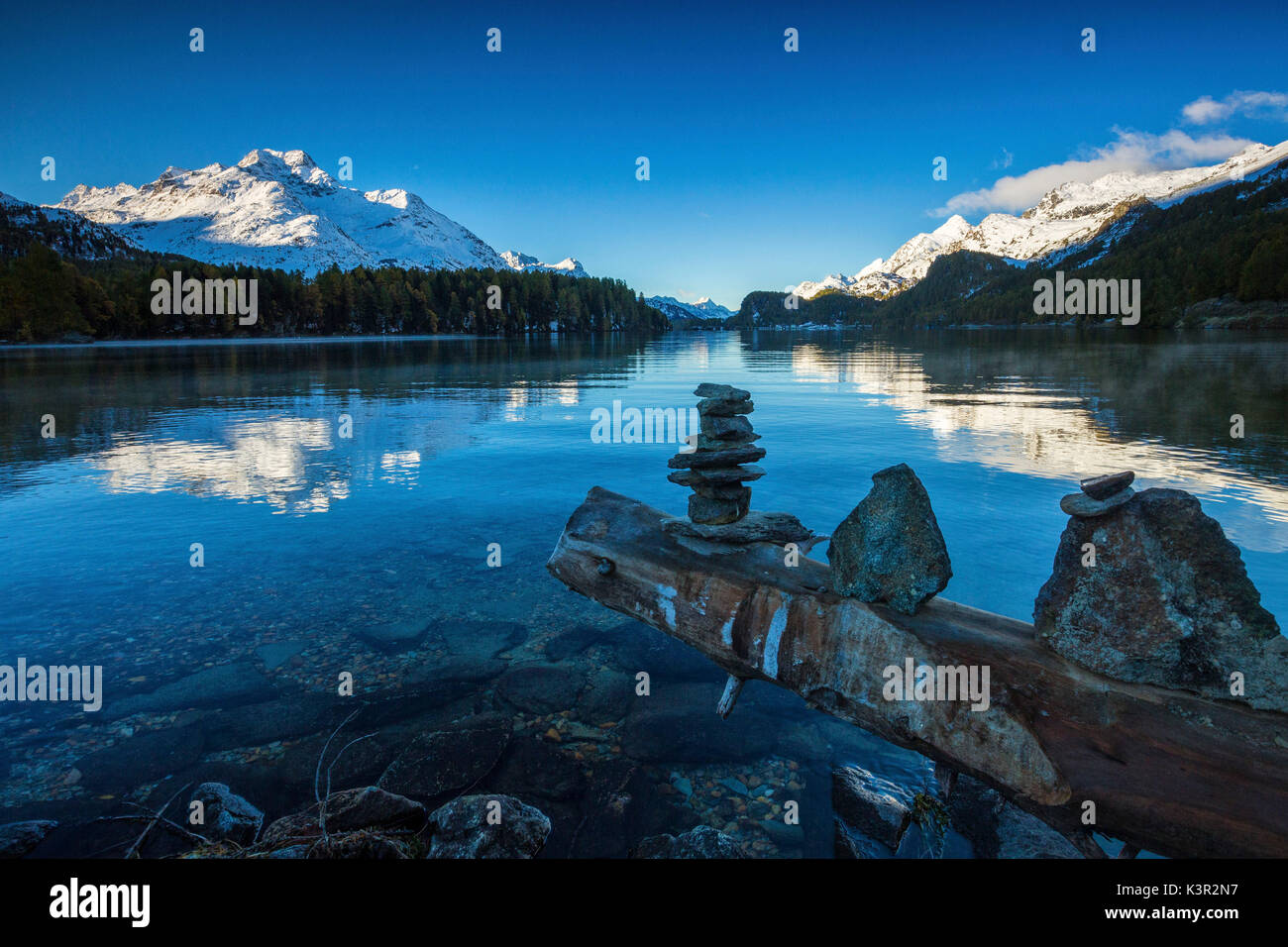 Dawn illuminates the peaks reflected in the calm waters of Lake Sils Engadine Canton of Graubünden Switzerland Europe Stock Photo