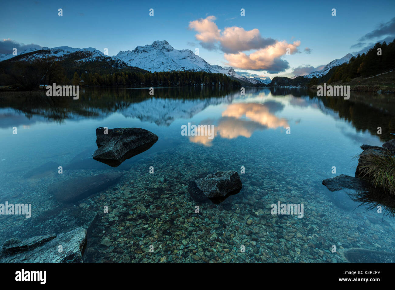 Dawn illuminates the peaks reflected in the calm waters of Lake Sils Engadine Canton of Graubünden Switzerland Europe Stock Photo