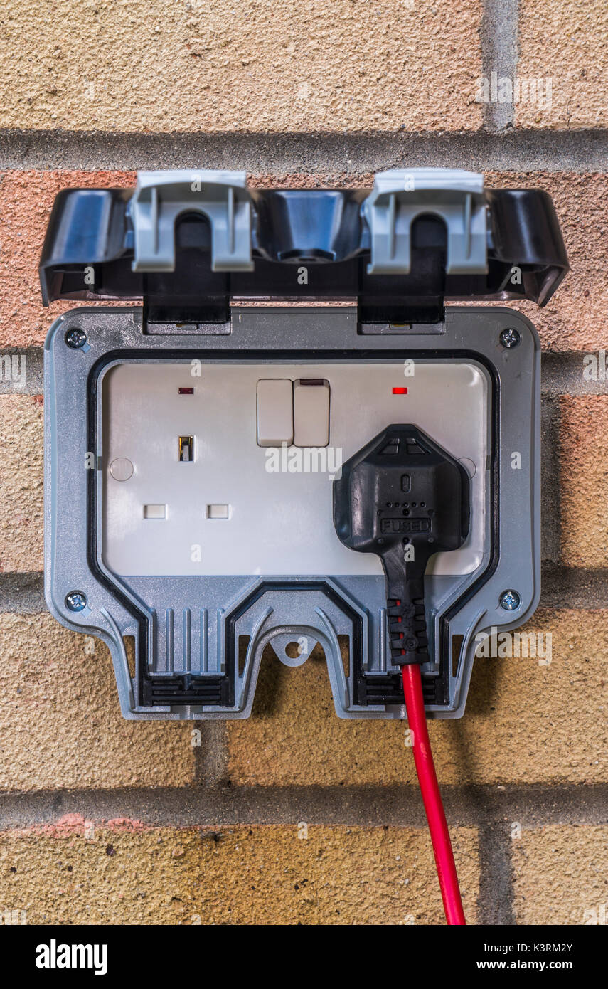Plug and lead in an outside power supply on a residential house wall,  mainly for garden use. Three pin, British, twin electrical sockets,  England, UK Stock Photo - Alamy