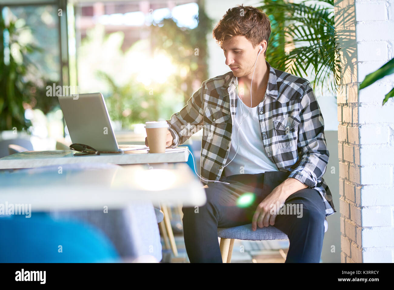 Portrait of pensive young man sitting at table in cafe using laptop Stock Photo