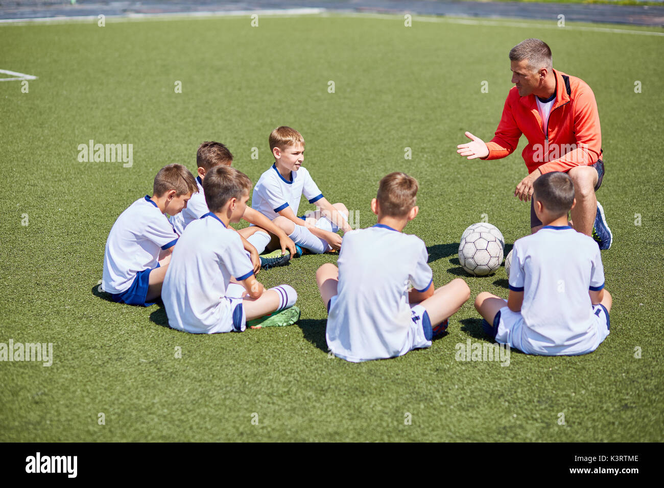 Portrait of boys team sitting in front of coach on football field