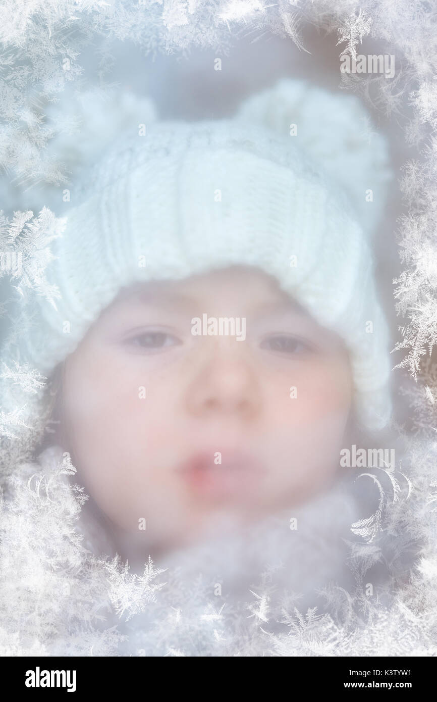 Child looks through iced window in winter Stock Photo