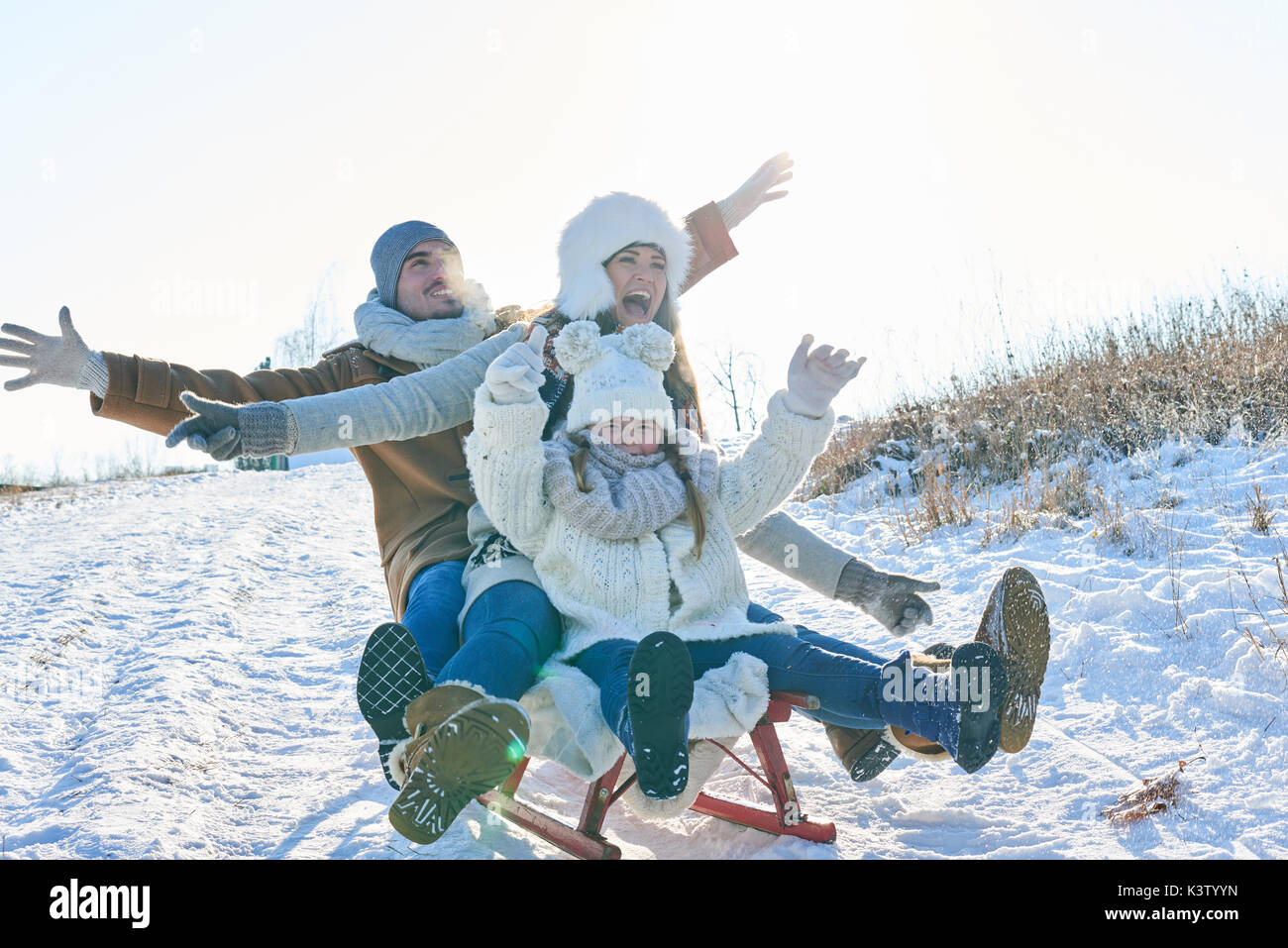 Family with parents and daughter playing toboggan in winter with enthusiasm Stock Photo