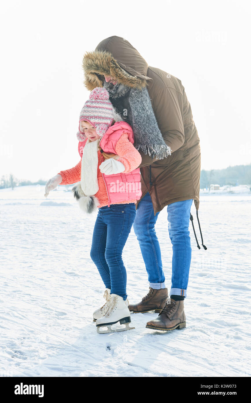 Father helps beginner child with ice-skating in winter Stock Photo