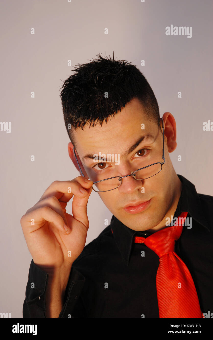 Young man wearing eyeglasses, looking at the camera thoughtfully. Stock Photo