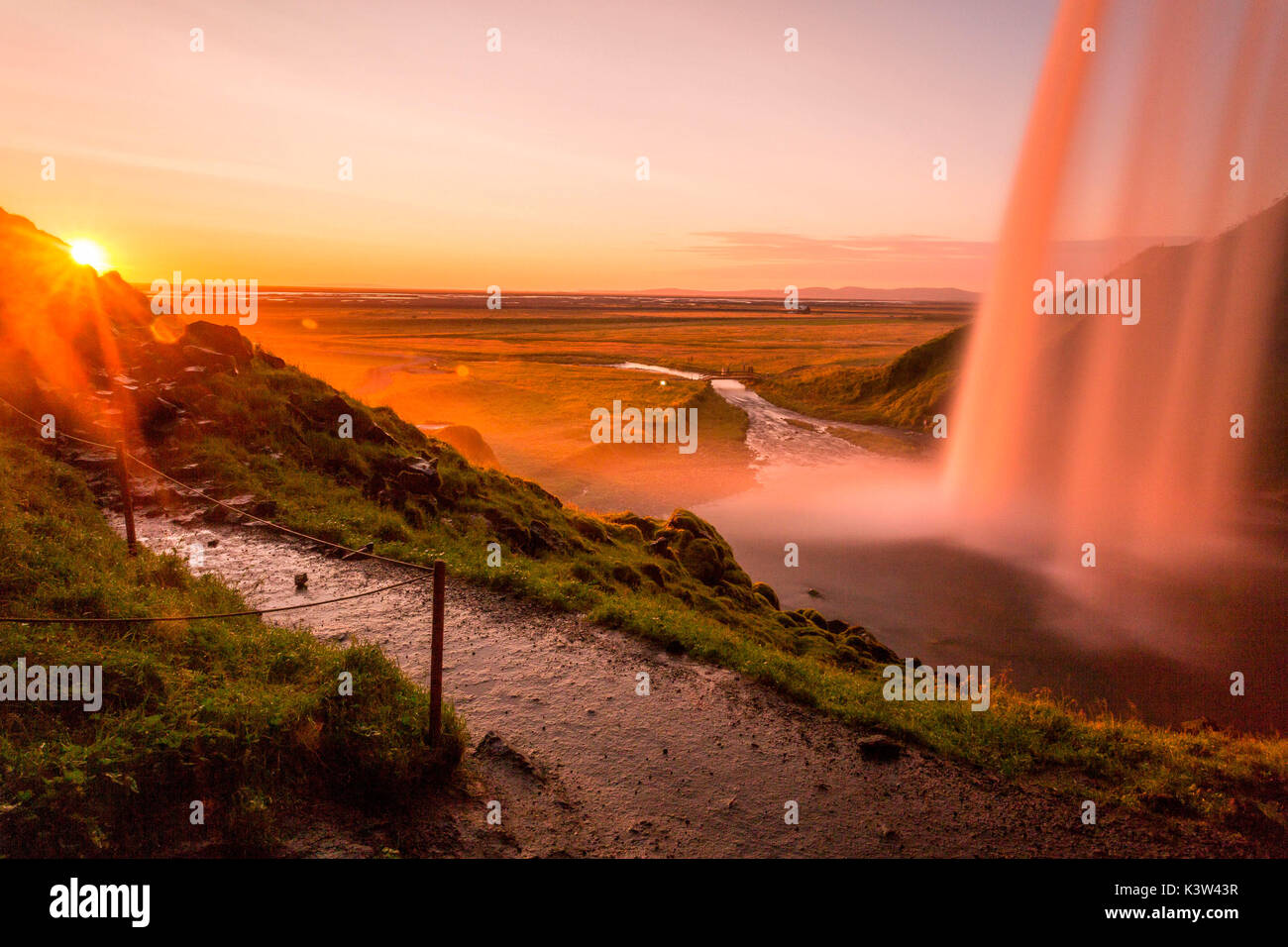 Iceland landscape, Seljalandsfoss waterfall at sunset, picture taken from behind the fall with sunburst Stock Photo