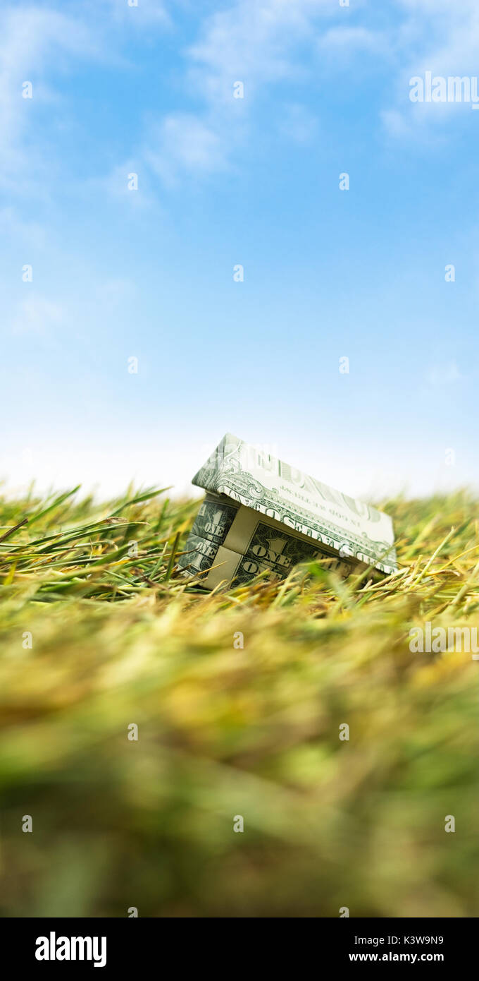 Housing Market crash. Sinking origami cash house on grass Stock Photo