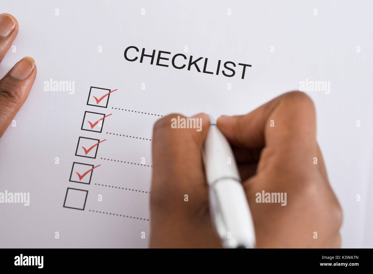 Person's Hand Marking Check Box With Red Pen On Checklist Form Stock Photo