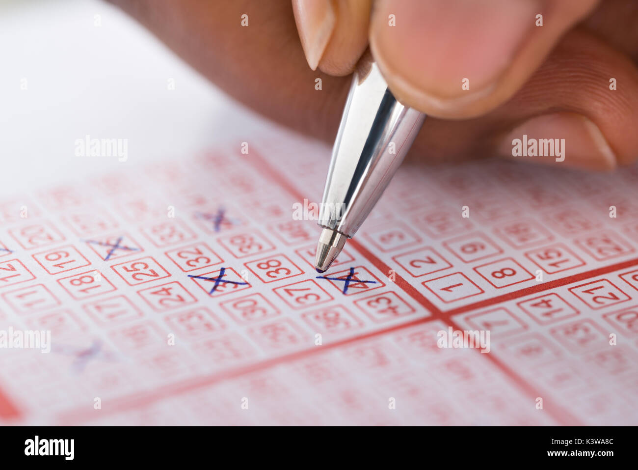 Close-up Of Person's Hand Marking Number On Lottery Ticket With Pen Stock Photo