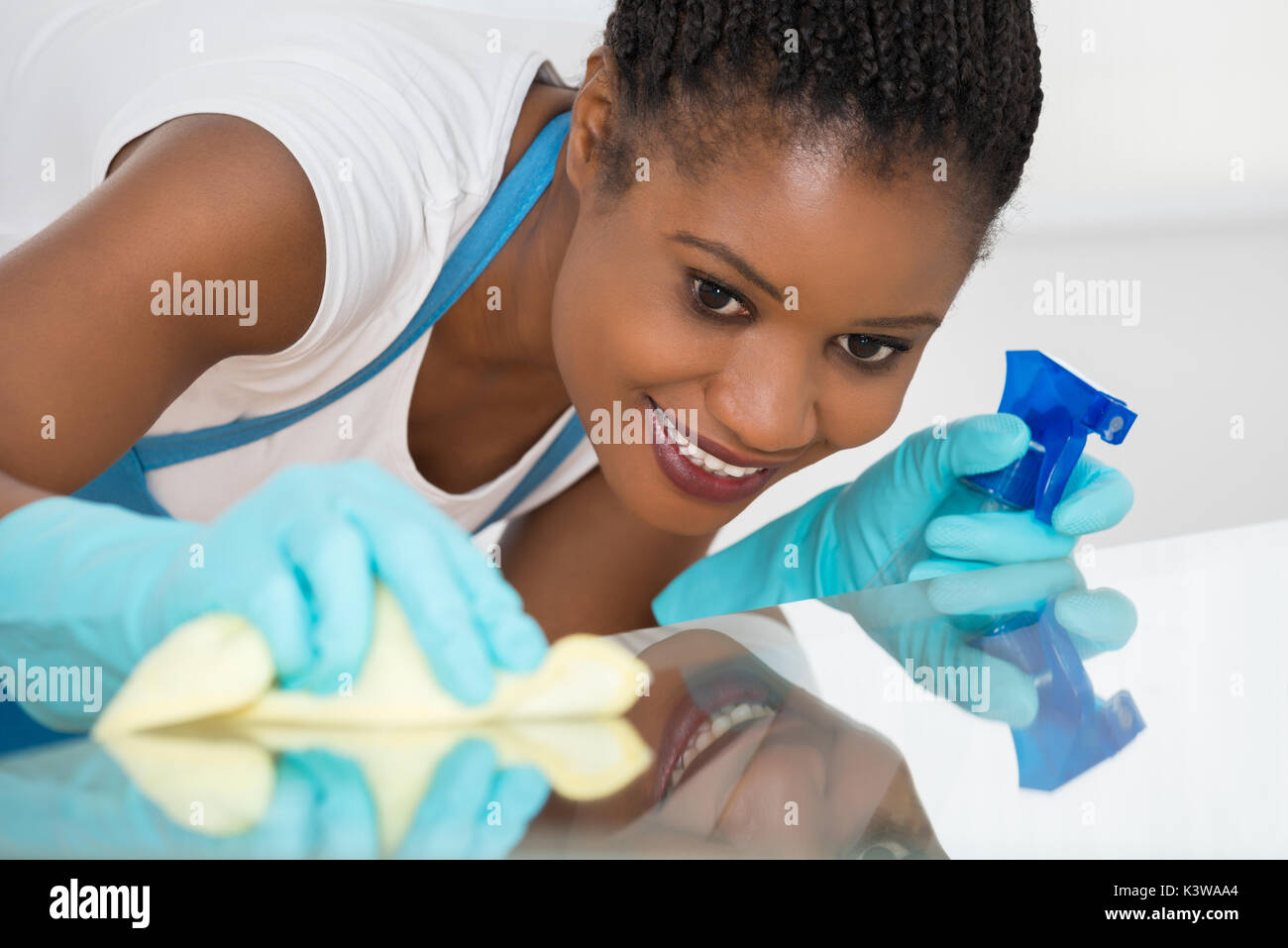 Close-up Of Young African Woman Using Spray To Wipe Glass Desk Stock Photo