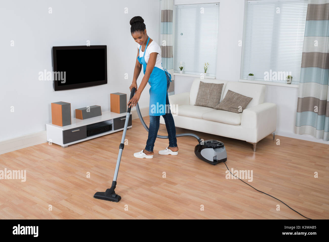 Young African Woman Cleaning Hardwood Floor With Vacuum Cleaner Stock Photo