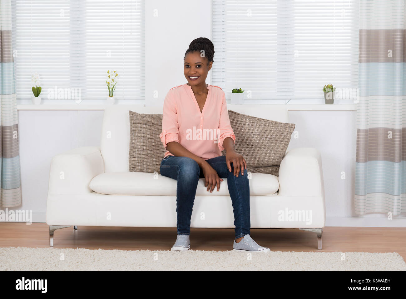 Smiling Young African Woman Sitting On Couch In Living Room Stock Photo ...